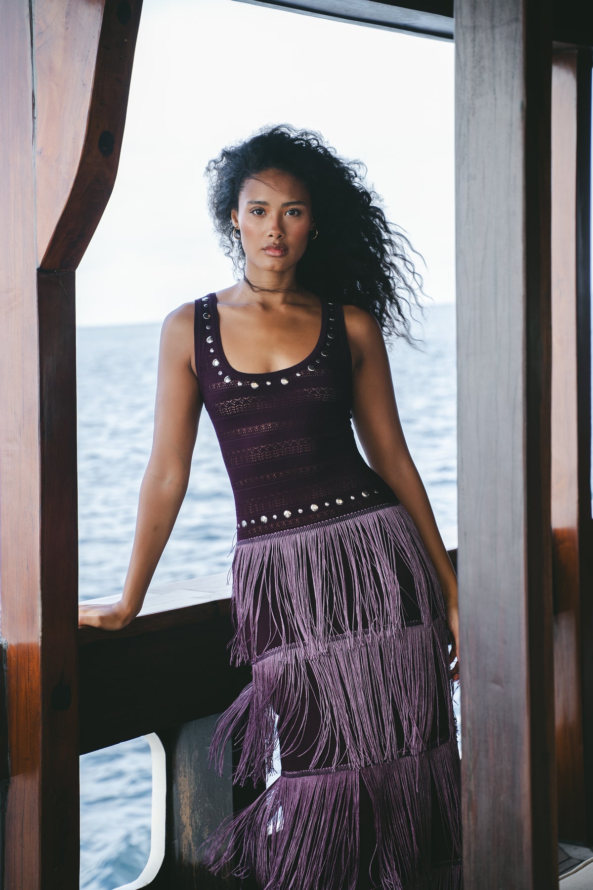 Model wearing the burgundy Fringe Knit Maxi Dress in a front view on a wooden boat.