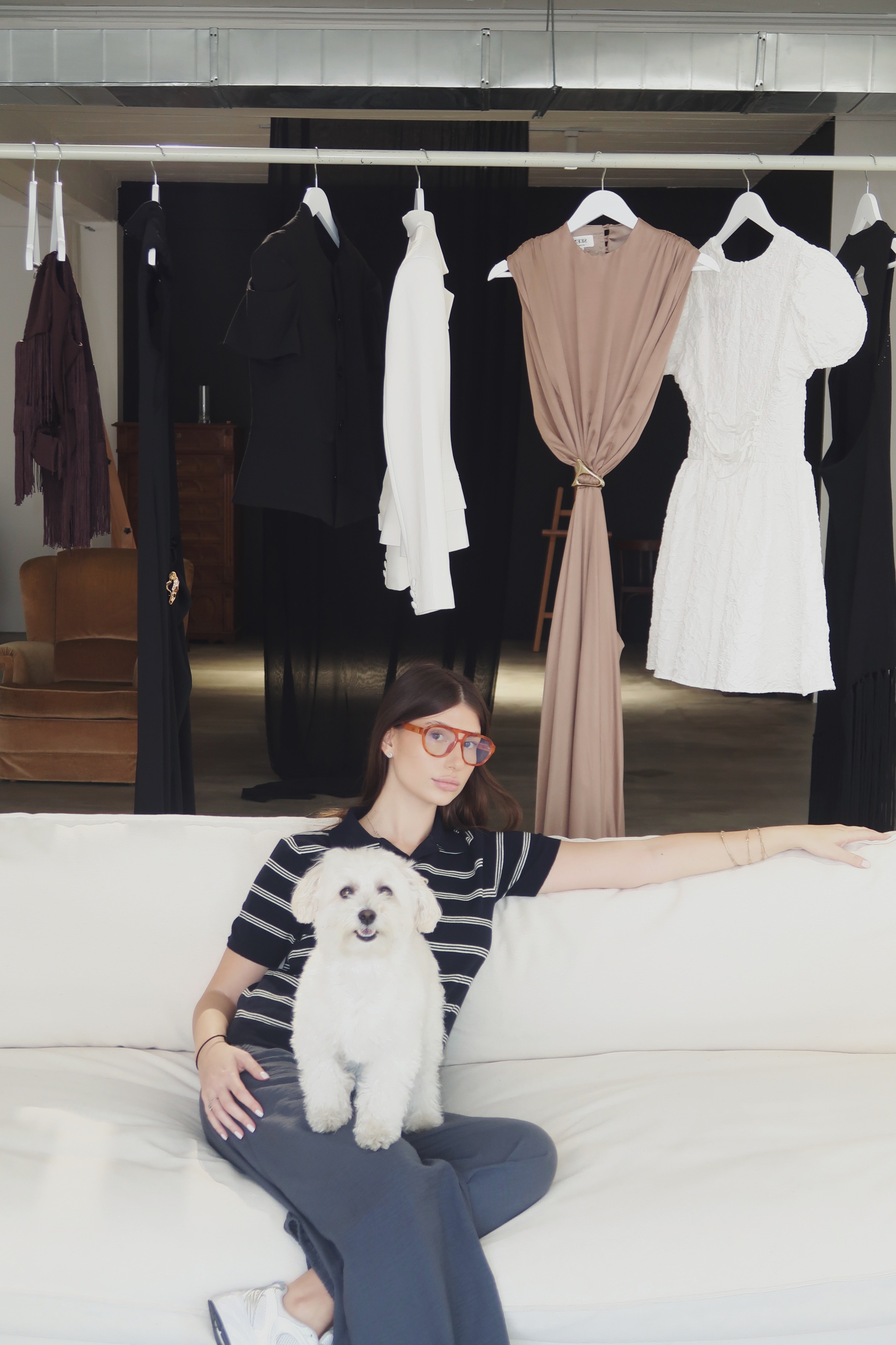 Nini seated in the Seen Studios workspace beneath a rail of garments