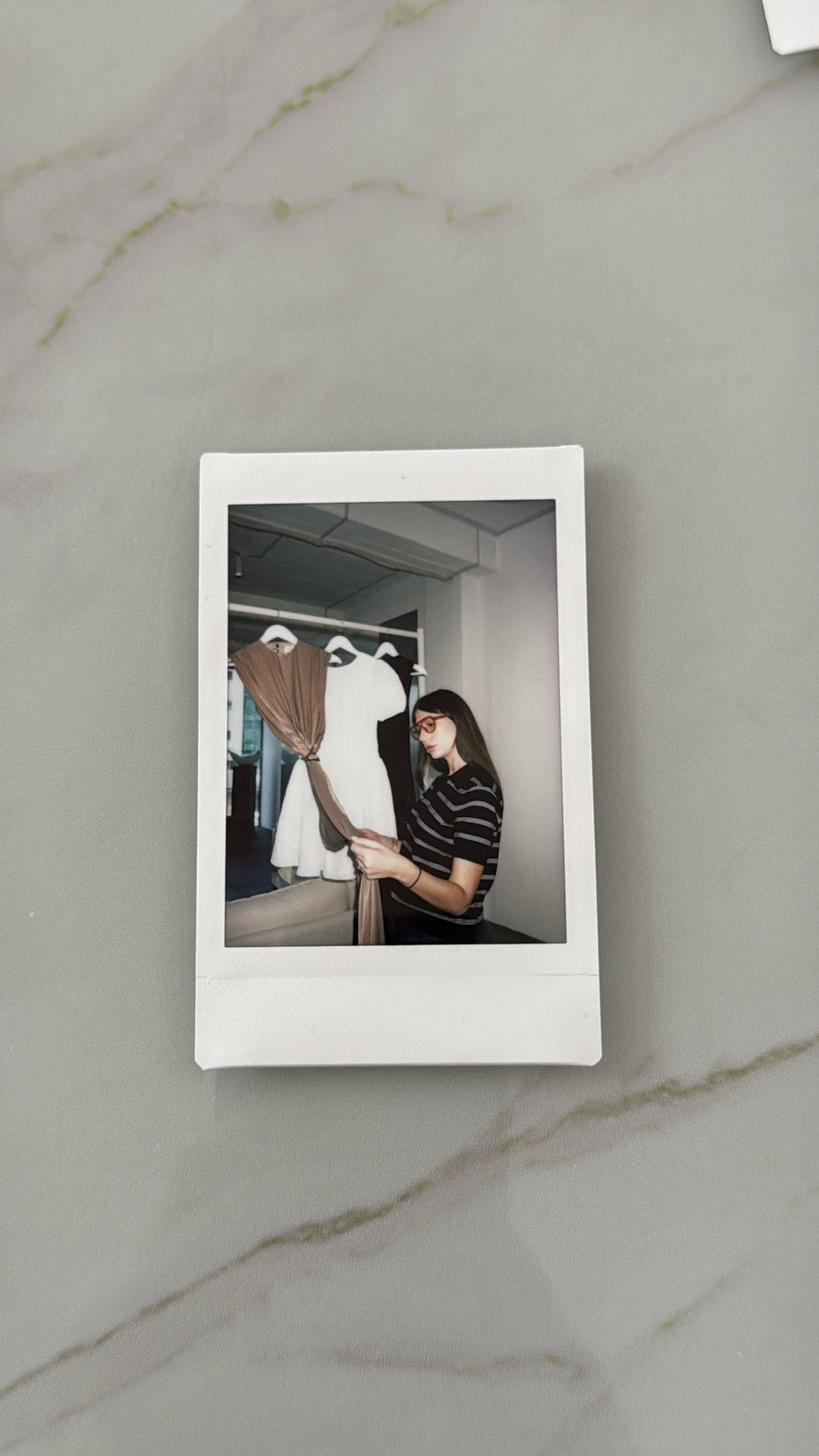Nini reviewing a draped garment beside white samples in the Seen Studios studio, photographed as a Polaroid on marble
