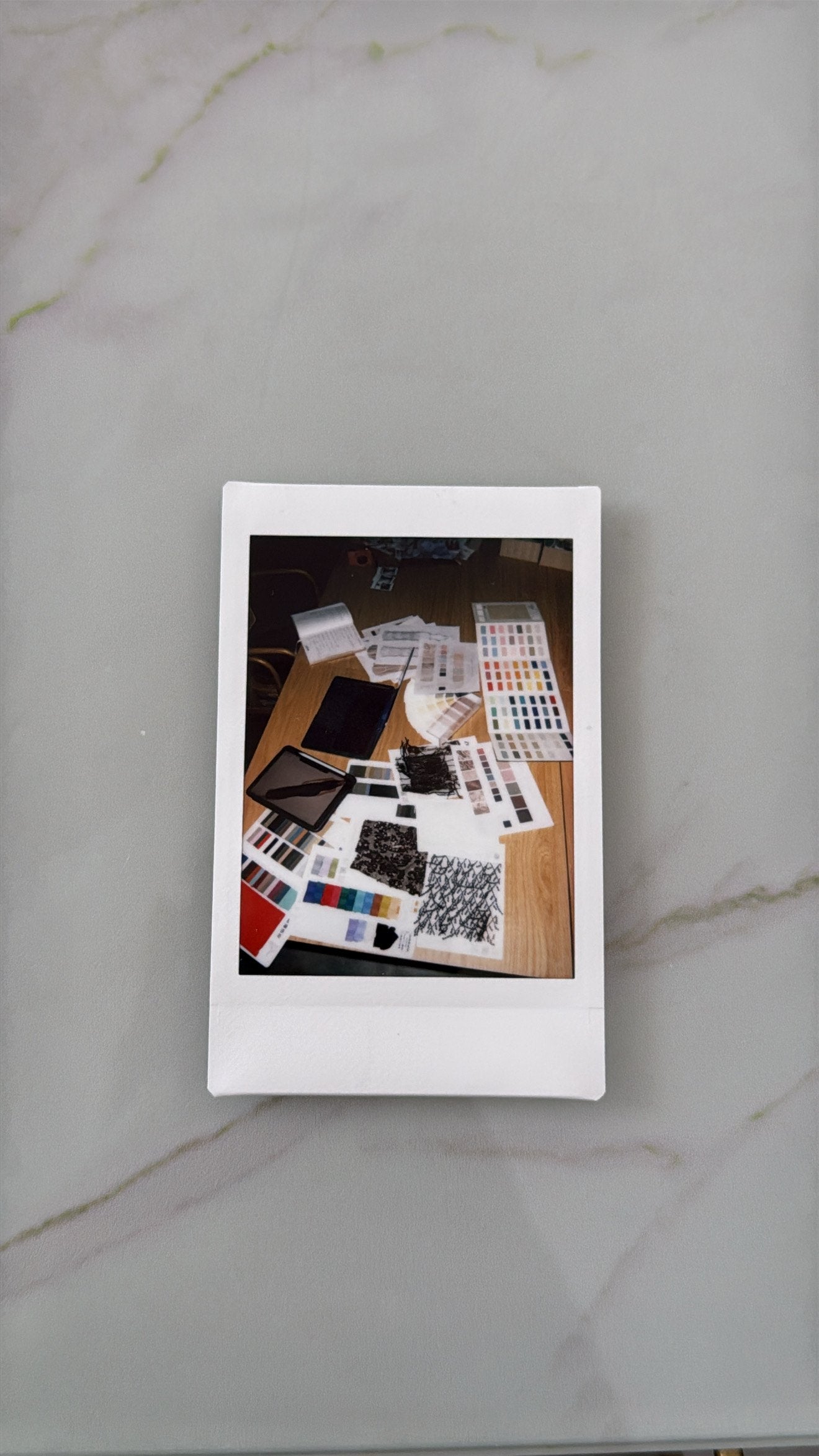 A Polaroid of fabric samples, lace, colour cards and notes on a Seen Studios worktable