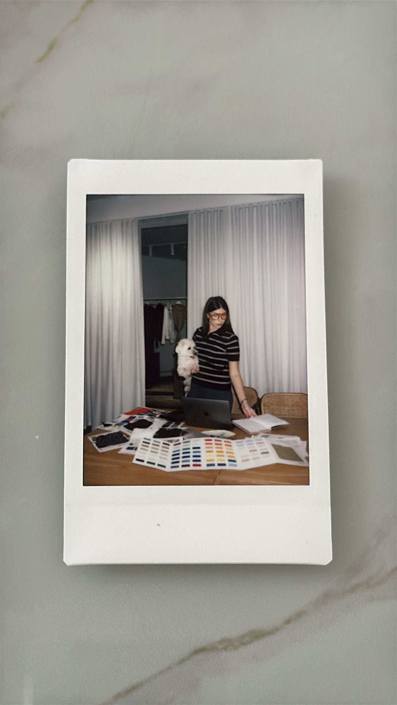 Nini editing colour and material references at the studio table with her dog, photographed as a Polaroid